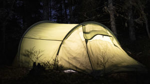 Valaistu teltta pimeässä metsässä.