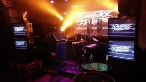 Synthar och skärmar på scenen före en av Flashback Future-klubbarna. En scen på en av flashback future festerna. Många crt skärmar och synthar på scenen.