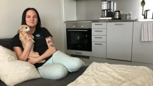 Jenni Vainio siivoaa lähes joka päivä. Kodin pinnat kiiltelevät ja kodissa valitsee raikas tuoksu. Nainen istuu koira sylissään sängyllä keittiössä.