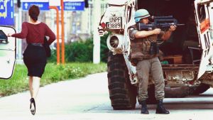En kvinna i höga klackar springer över Sniper Alley i Sarajevo medan en fransk fredsbevarare försöker ge skydd. En kvinna i höga klackar springer över Sniper Alley medan en fransk fredsbevarare försöker skydda henne.