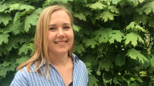 Jannica Lindqvist säger att man inte behöver någon sommarstuga om man bor på landet eller i skärgården och har nära till havet. jannica lindqvist i blåvitrandig skjorta framför en lövbuske