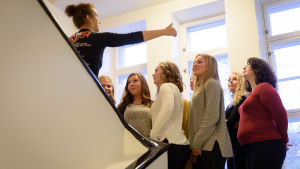 Luciakandidaterna dirigeras av fotograf för den första gruppbilden. Luciakandidater står i trappuppgång och dirigeras av fotograf för gruppbild.