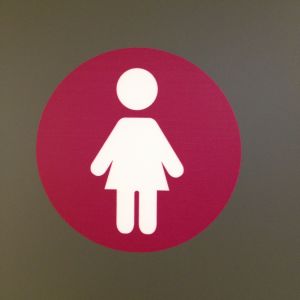 Tohlopin mediapoliin naisten wc:n luumunpunaruskea ja valkoinen logo, nainen pallossa.
