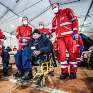Röda korset-anställda i ett fältsjukhus. En man i rullstol sitter bredvid dem.