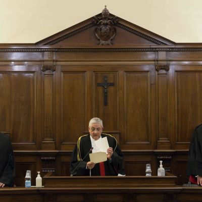 Kolme röyhelökauluksista tuomaria seisoo krusifiksillä varustetun puisen paneelin edessä