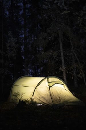 Valaistu teltta pimeässä metsässä.