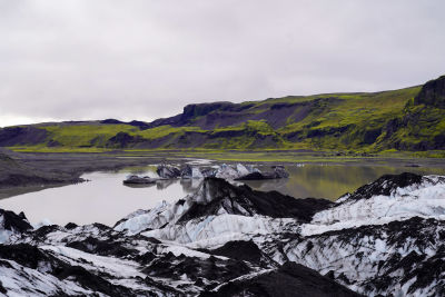 Glaciär i förgrunden, gröna berg i bakgrunden.