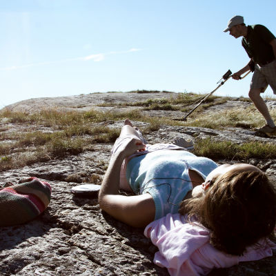 Isä etsii aarretta, tytär lekottelee kalliolla elokuvassa Isot ihmiset