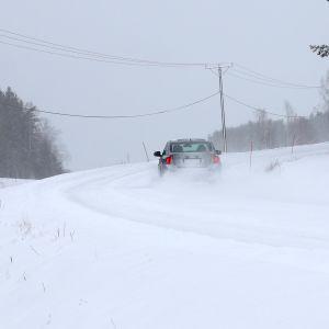 En bil kör in i en kurva på en snöig väg.