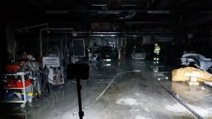 En bilverkstad där det brunnit är helt svart. En strålkastare lyser upp golvet och bilar.