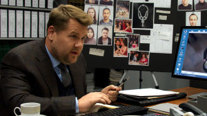 James Corden dyker upp i rollen som misstänksam försäkringsagent. Närbild på John (James Corden) som sitter vid ett skrivbord.