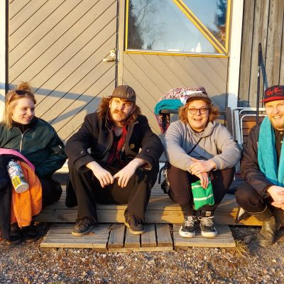 Fyra personer i bandet Bad Sauna sitter på en trappa, på väg mot bastun. De ser glada ut.
