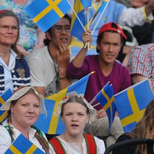 Svenskar sitter i läktare med Sverigeflaggor och firar nationaldag.