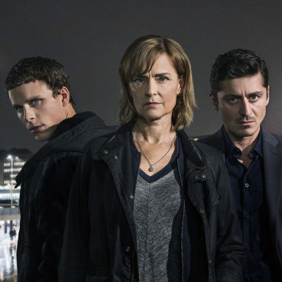 Seriens tre huvudpersoner iförgrunden med en nattmörk stad i bakgrunden.