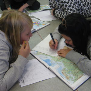 Kaksi tyttöä tekee luokan lattialla tehtäviä kartan kanssa.