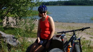 Maarit Tuomisto, chef för biblioteks- och fritidstjänster, är kanske en av Sjundeåborna som önskar sig nya cykelleder. Maarit Tuomisto vid en strand med cykelhjälm på huvudet och en cykel bredvid sig.
