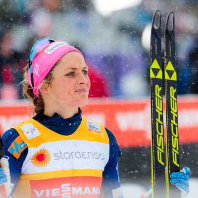 Therese Johaug med skidor i vänster hand och stavar i höger hand.
