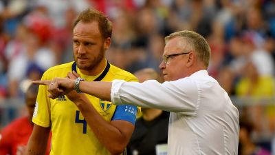 Janne Andersson i vit skjorta förklarar saker för sin gulklädda spelare Andreas Granqvist.