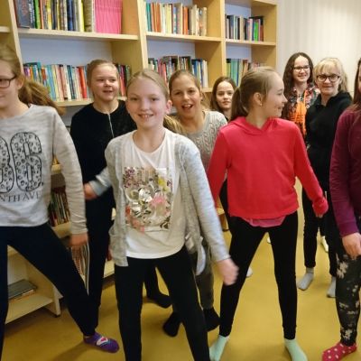 Tytöt tanssivat koulun kirjastossa.