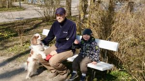 Halva familjen Liigsoo på en parkbänk i Kuressaare. Pappa Liigsoo med sin son och hunden Lotte sitter på en parkbänk i Kuressaare på Ösel i Estland.