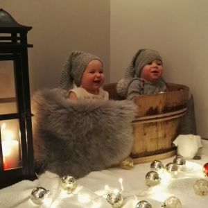 Två små barn sitter i en korg med tomteluva på