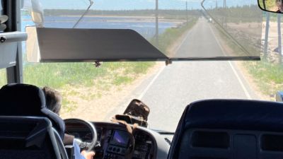 Vy genom framfönstret i en buss. Asfaltsväg med vatten på båda sidor.