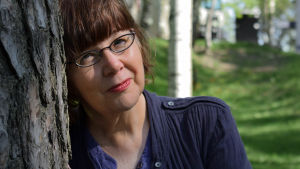 Camilla Thelestam har stått för radiobearbetningen och regin av White Monkey Dramaturgen Camilla Thelestam lutar mot en tall med sommargrönska i bakgrunden.