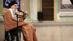 Ali Khamenei, en äldre man med grått skägg sitter i en stol och talar i en mikrofon.