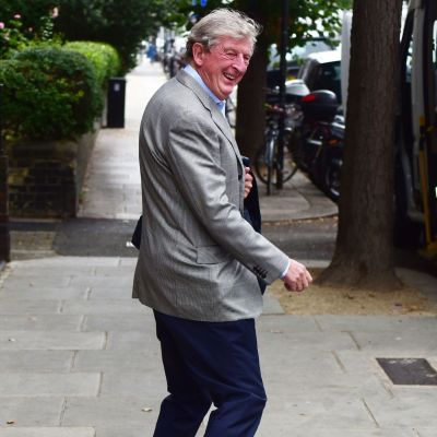 En skrattande Roy Hodgson i grå kavaj promenerar på en gata.