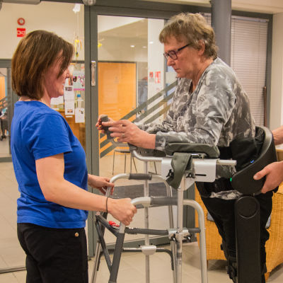 Maj-Len Sjöberg testar gångroboten Indego. Fysioterapeuterna Daniel Söderman och Katri Pihlaja-Kuhna assisterar.