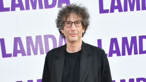 Neil Gaiman är en av finalisterba. Neil Gaiman klädd i svarta kläder. Står framför en vägg som det står LAMDA på.