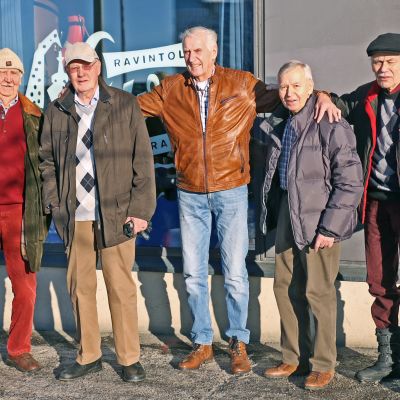 Viisi vanhaa miestä seisoo ravintolan edustalla kädet toistensa harteilla