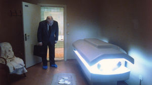 Hallå är det någon hemma? Ur comebackfilmen "Sånger från andra våningen". en man i kostym lutar sig över ett solarium ur vilket en mans bara fötter sticker fram.