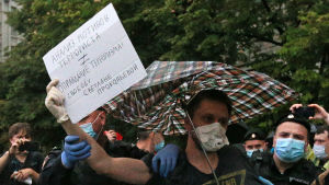 Polisen grep flera demonstranter som uttryckte sitt stöd för Prokopjeva utanför FSB:s högkvarter i Moskva den 3 juli. "Analys av en terrorists motiv är inte samma som att rättfärdiga terrorism", står det på plakatet. En man under paraply håller en skylt, poliser i bakgrunden fattar tag om honom.
