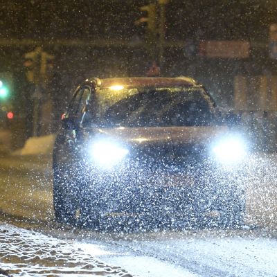 En bil med starka framlyktor kommer körande längs en snöig Nordenskiöldsgata i Helsingfors.