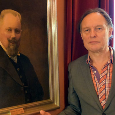Konstnären Peik Bäckström står bredvid porträttet av borgmästare Harry Winqvist.