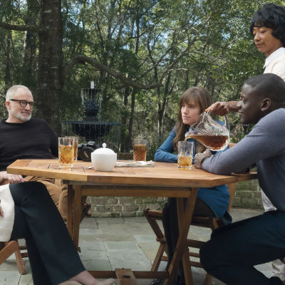 Chris (Daniel Kaluuya) sitter tillsammans med Rose (Allison Williams) och hennes familj vid ett altanbord och dricker ice tea.