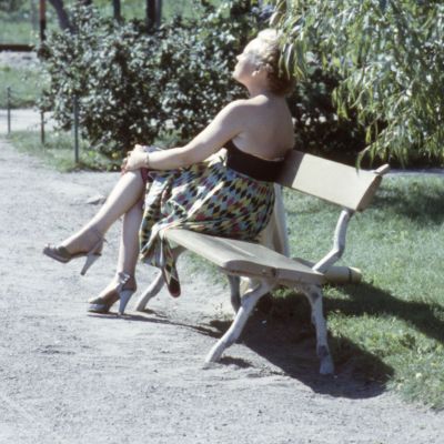 Nainen istuu puistonpenkillä aurinkoa ottaen.