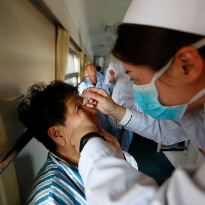 Hoitaja antaa potilaalle silmätippoja ennen leikkausta Jilin maakunnassa Kiinassa. Hoito tapahtuu hyväntekeväisyysjärjestön operoimassa junassa, joka kiertää Kiinan syrjäseutuja tarjoten varattomille maksuttomia silmäleikkauksia. Kuva elokuulta 2017.