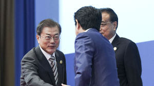 Stämningen såg förhållandevis god ut då de två ledarna möttes i Kina. Två män skakar hand med varandra. Shinzo Abe ser på Moon Jae-in.