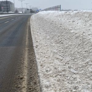 Trottoar intill bilväg som närmast helt är täckt av en smutsgrå snövall. 
