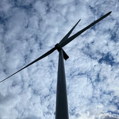 en bild av en vindmölla taget från marken så man ser rotorbladen och den molniga himlen