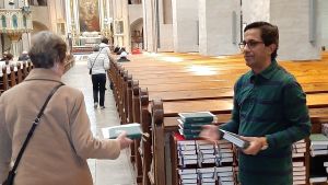 Många av de trognaste kyrkobesökarna hör till riskgrupper, men kan också fortsätta följa gudstjänster över nätet. Fayyah Alessa, en man med glasögon och grön skjorta, ger en psalmbok till en kyrkobesökare inför högmässan i Åbo Domkyrka.