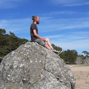 Man sitter på en stor sten på en strand.