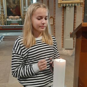 Cecilia Mäki-Kuutti tänder under högmässan ett ljus för de avlidna. Cecilia Mäki-Kuutti, en flicka med långt ljust hår och en svartvitrandig skjorta, tänder ett ljus i Åbo domkyrka.