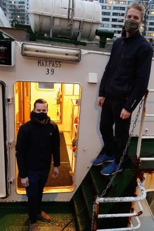 Gustav Ramberg och Jonas Skrifvars ombord på M/S Hamnskär. Gustav Ramberg och Jonas Skrifvars, två unga män med munskydd, står då däcket och i en lejdare ombord på en sjöbuss en vintermorgon.