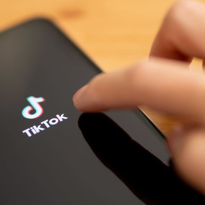 Sormi, joka osoittaa kännykän ruudulla näkyvää Tiktokin logoa.