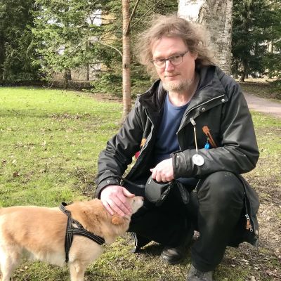 Johanni Larjanko klappar sin hund. Parkmiljö.