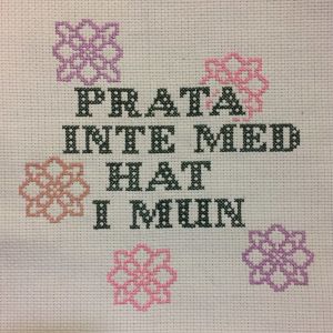 Korsstygnsbroderi med texten: prata inte med hat i mun