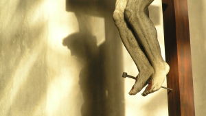 Fötterna med spik igenom, detalj av Jesus på korset. På väggen skugga av Jesus ansikte i profil och törnekronan på huvudet.